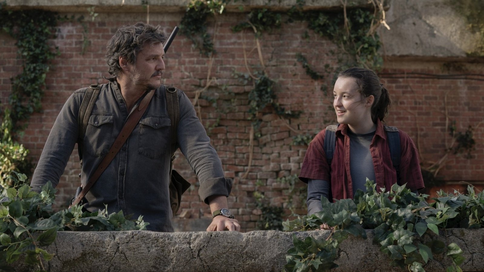 Joel and Ellie from “The Last of Us” smile at each other on a dilapidated brick balcony.