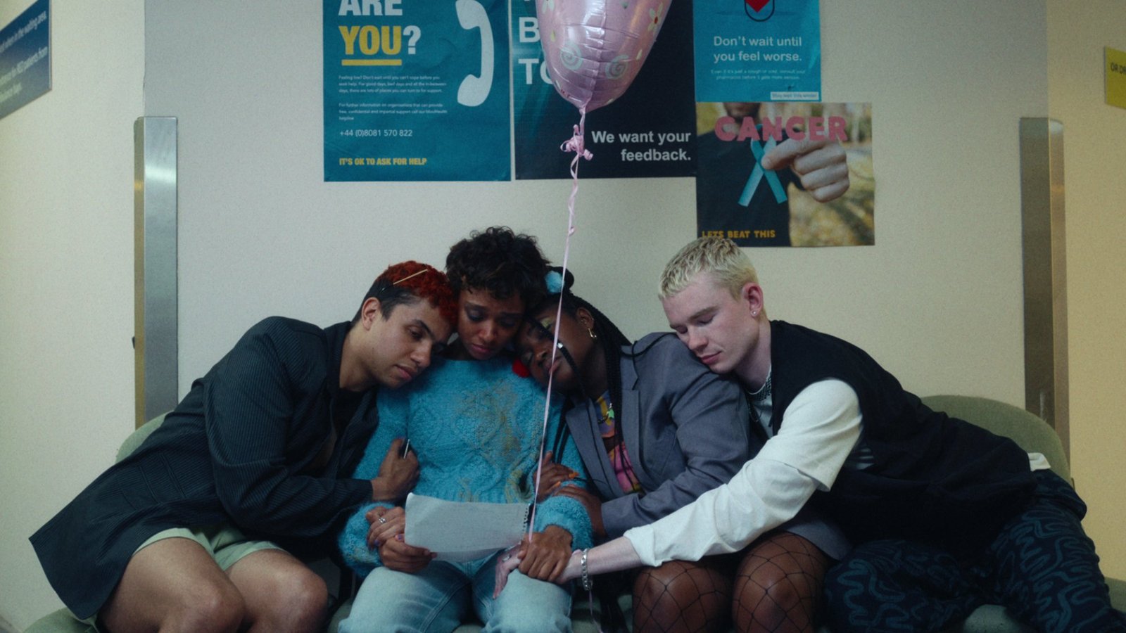 Four teens hug holding a piece of paper and a balloon.